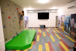 Una pared de escalar con presas de colores, un colchonete verde acolchado y un televisor de pantalla plana en la pared.