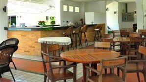 Un espacio interior amplio con techo alto, varios ventiladores de techo, una mesa de madera central rodeada de sillas y una zona de bar con taburetes.