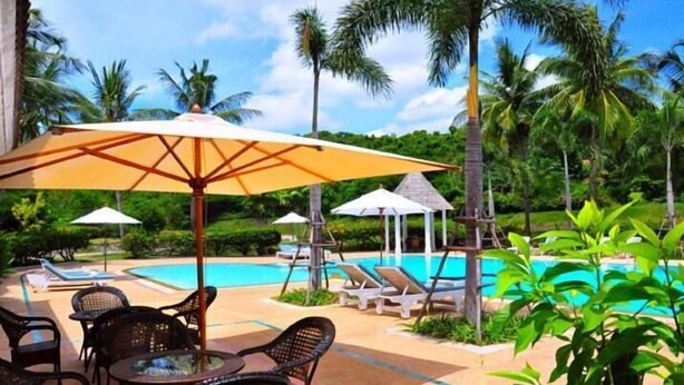 Un área junto a la piscina con sillones de descanso, sombrillas y una mesa.