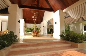 A covered outdoor area with steps leading to a central seating area, surrounded by white walls and greenery.