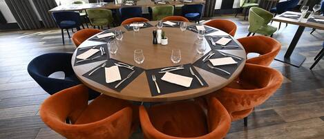 Un salón de conferencias con una mesa redonda dispuesta para una reunión, rodeado de sillas naranjas.