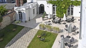 A courtyard with outdoor seating and a white building with multiple windows. - Manoir de l'évêché et Spa (Lisieux)