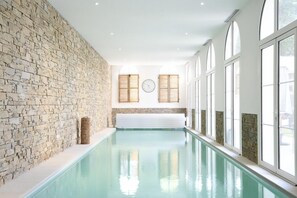 A long indoor swimming pool with stone walls and large windows. - Manoir de l'évêché et Spa (Lisieux)