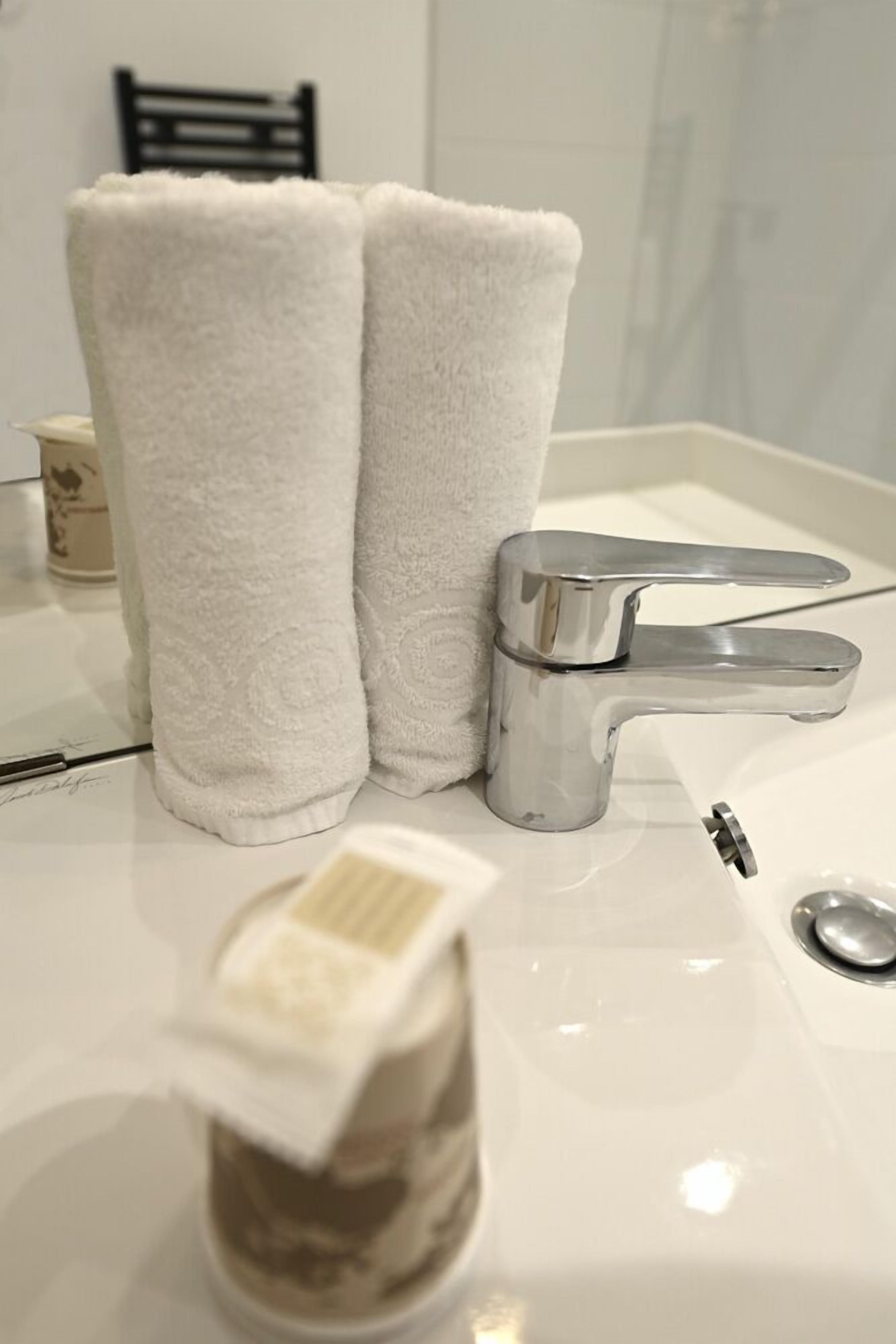 A bathroom with a white sink, a chrome faucet, and two white towels.