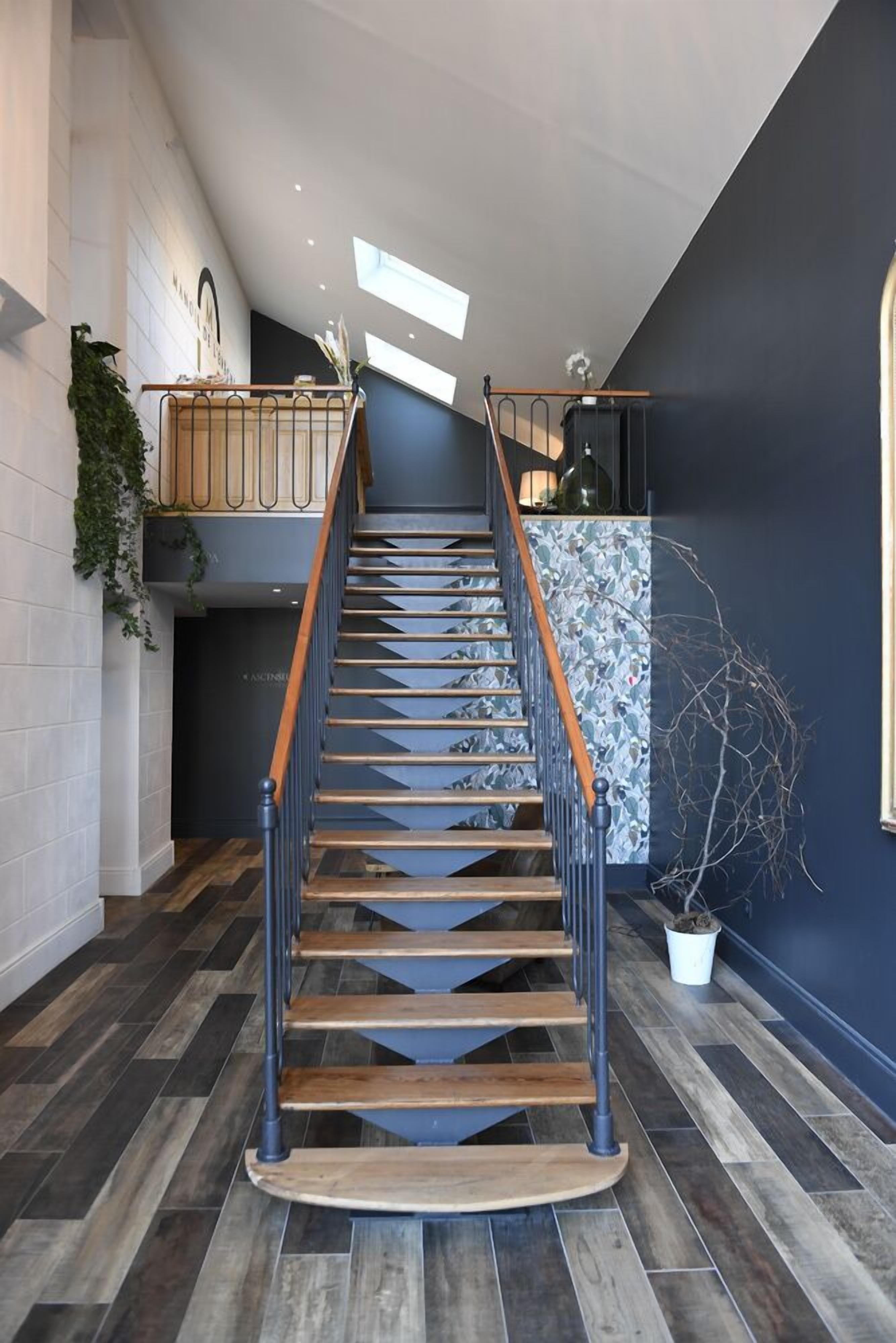 A modern staircase with wooden steps and black railings, leading to a landing with a dark wall and a window.