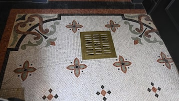 Een gedetailleerde mozaïekvloer met bloemmotieven en een afvoer in het midden.