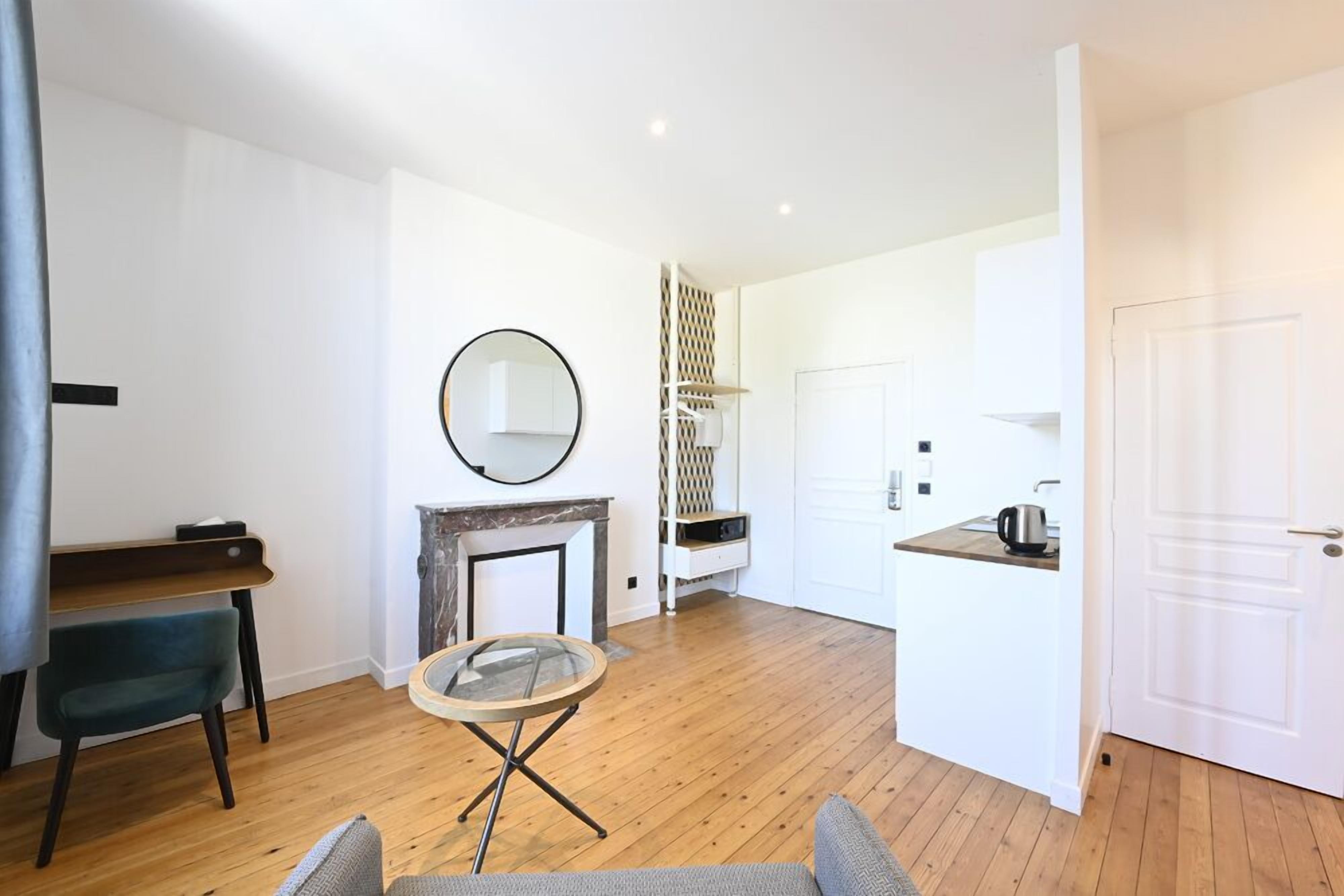 Een moderne woonkamer met een open haard, een ronde spiegel, een klein rond tafeltje en een bank.