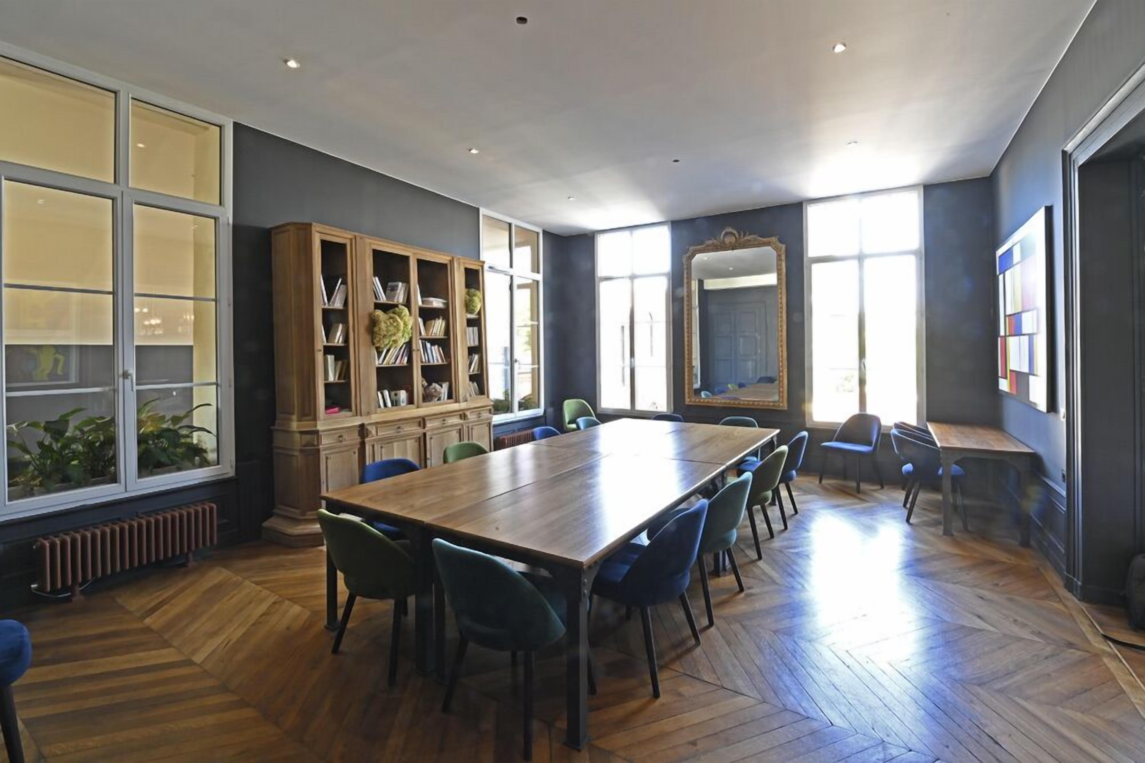 A conference room with a long table, chairs, a bookshelf, and large windows.