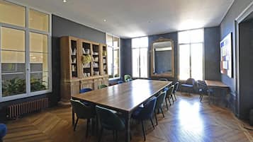 A conference room with a long table, chairs, a bookshelf, and large windows.