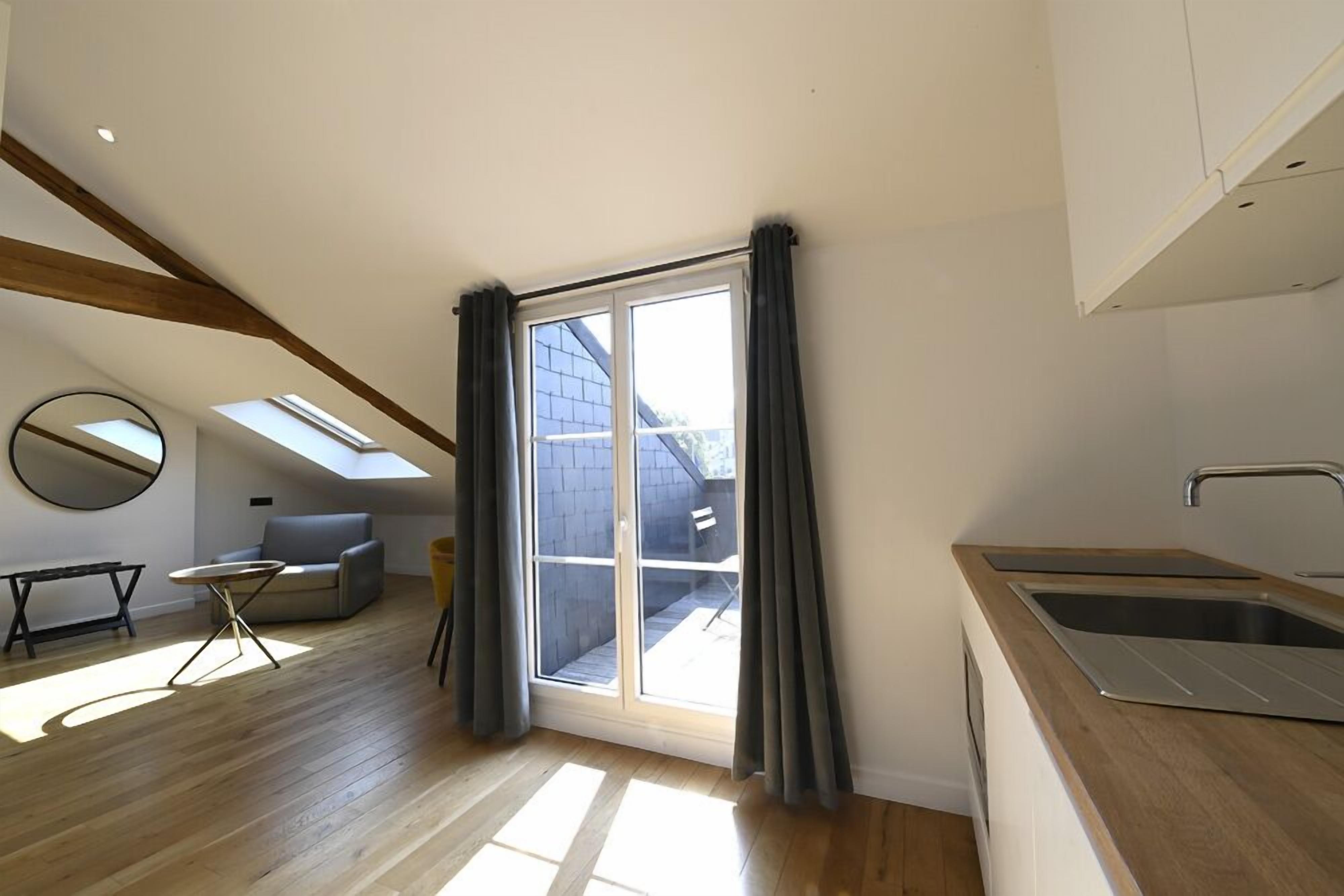Eine moderne Küche mit großem Fenster, ein Essbereich mit Tisch und Stühlen sowie ein Schlafschlafzimmer im oberen Bereich mit Dachfenster.