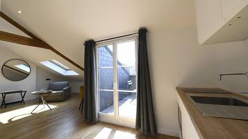 Eine moderne Küche mit großem Fenster, ein Essbereich mit Tisch und Stühlen sowie ein Schlafschlafzimmer im oberen Bereich mit Dachfenster.