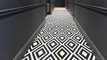 A hallway with a geometric patterned floor, dark walls, and recessed lighting.