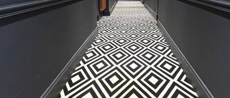 Un pasillo con piso de diseño geométrico, paredes oscuras e iluminación empotrada.