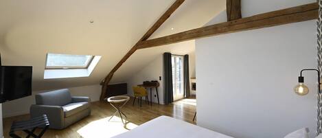 A modern loft bedroom with a sloped ceiling, a skylight, a bed, a sofa, a small table, and a TV.