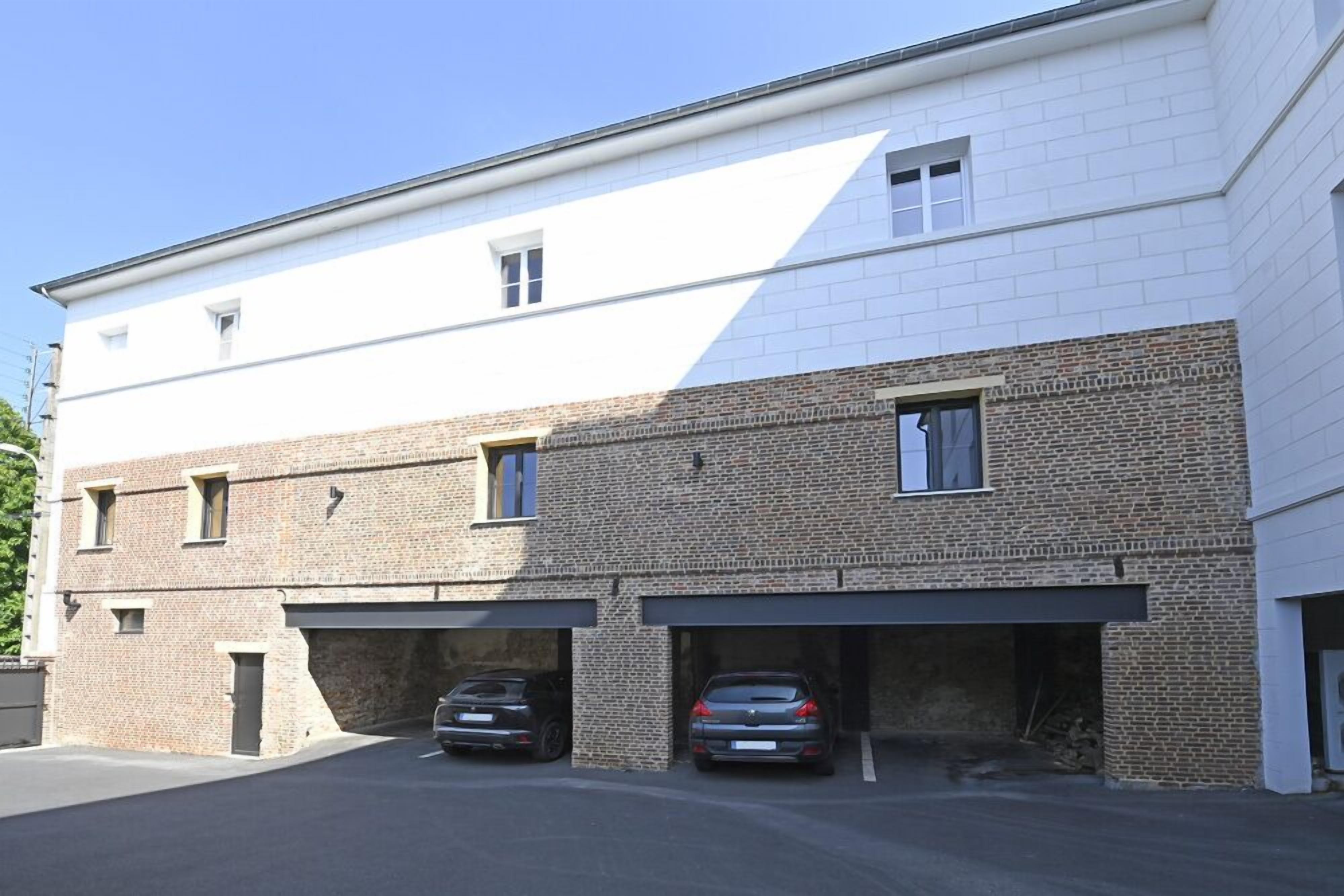 A two-story building with a white upper section and a brick lower section. There are two garages with cars parked inside.