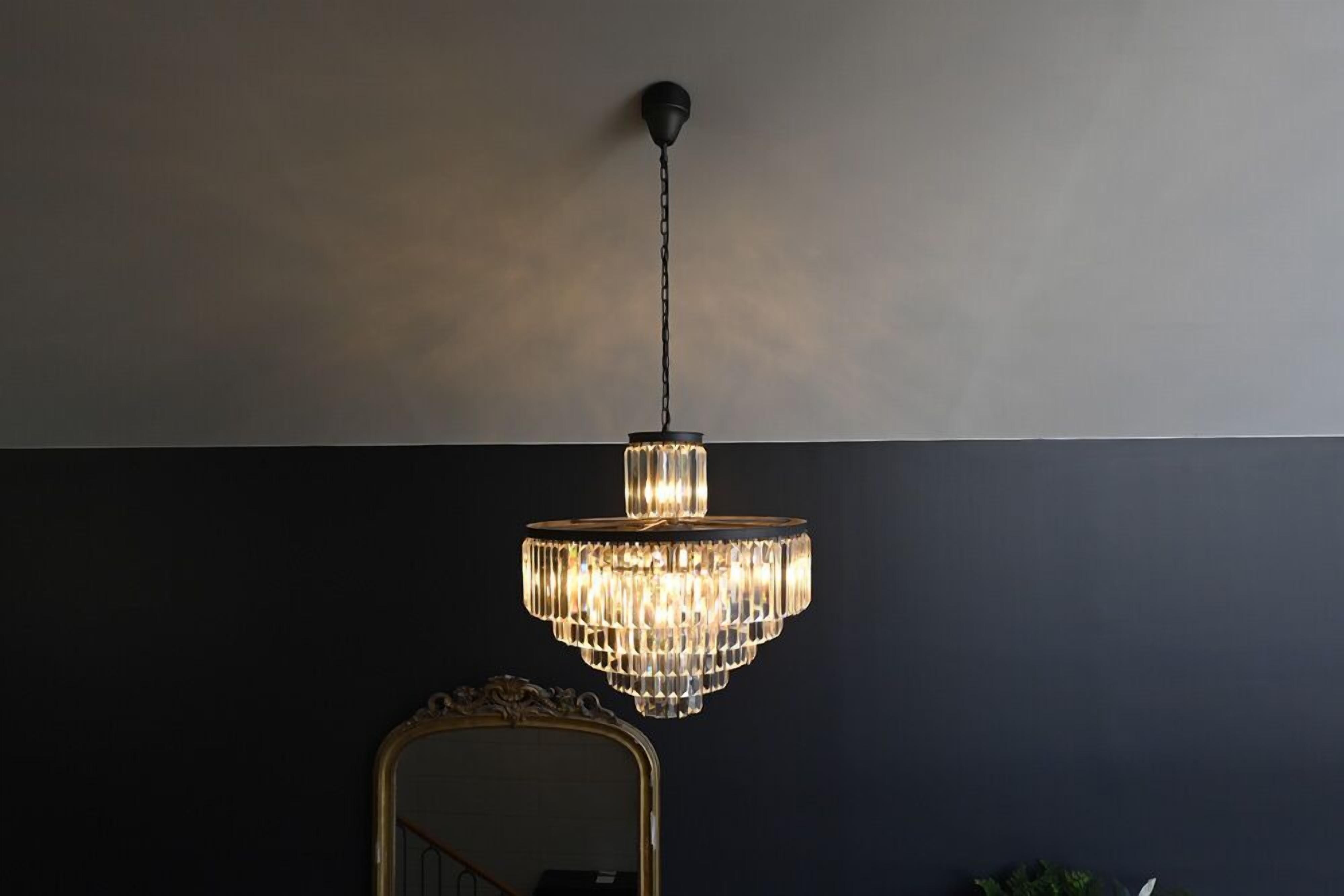 A chandelier hanging from the ceiling in a room with a dark wall and a gold-framed mirror.