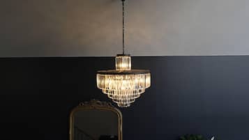 A chandelier hanging from the ceiling in a room with a dark wall and a gold-framed mirror.