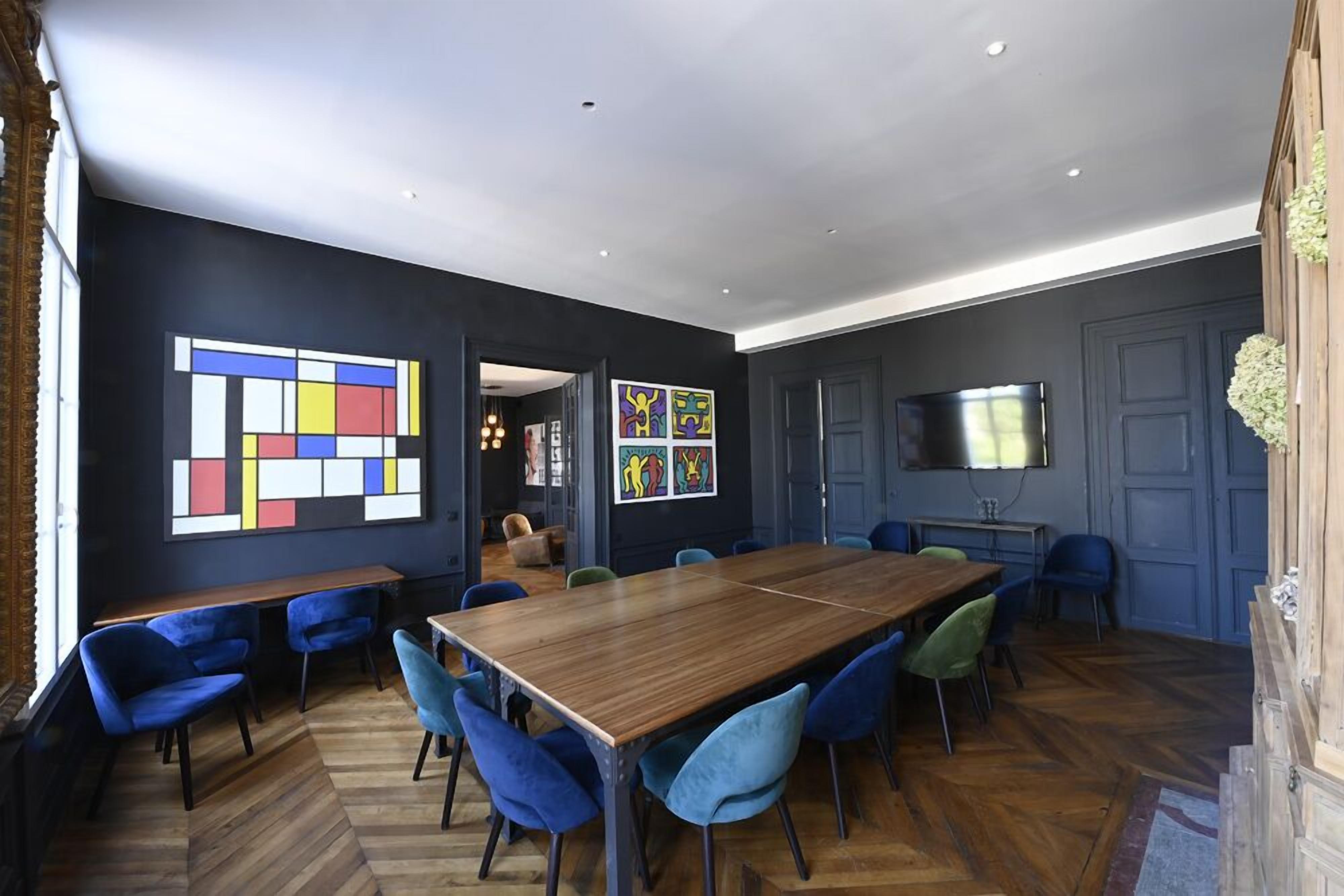 Un espace repas moderne avec une longue table en bois, des chaises bleues et des œuvres d’art accrochées aux murs.