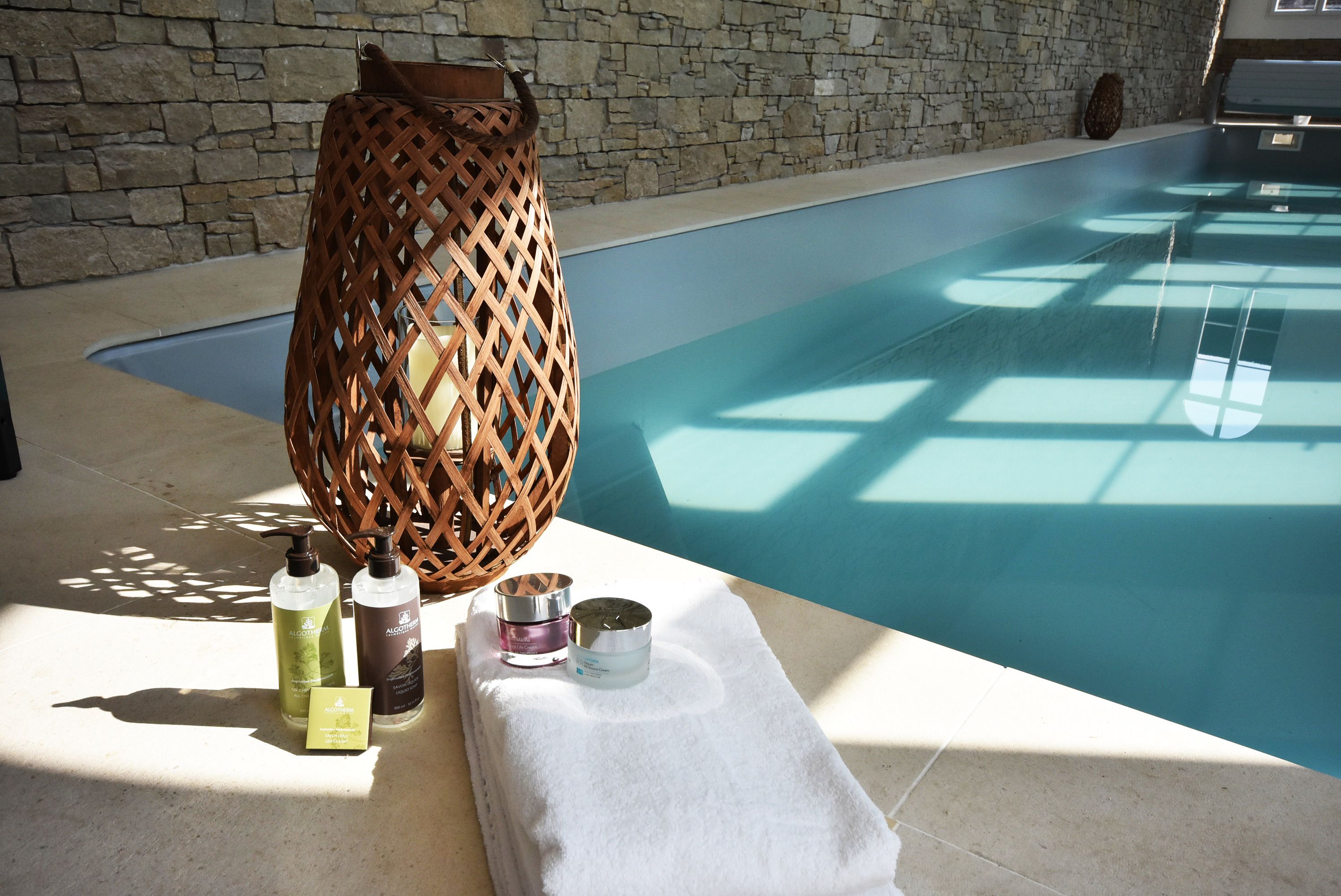 Un espace piscine agrémenté d’un mur en pierre, d’un panier tressé et de produits de soins pour la peau disposés sur une serviette.