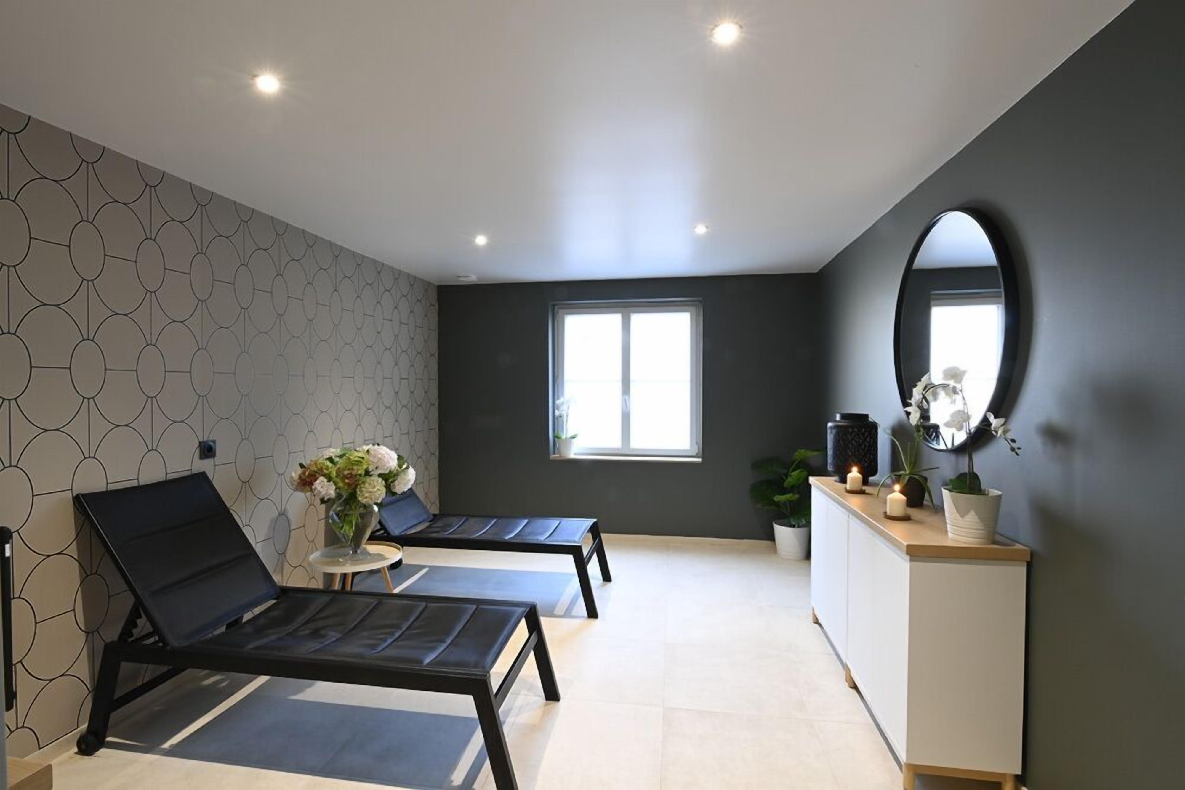 A modern room with two black lounge chairs, a small table with flowers, a large mirror, and a window providing natural light.