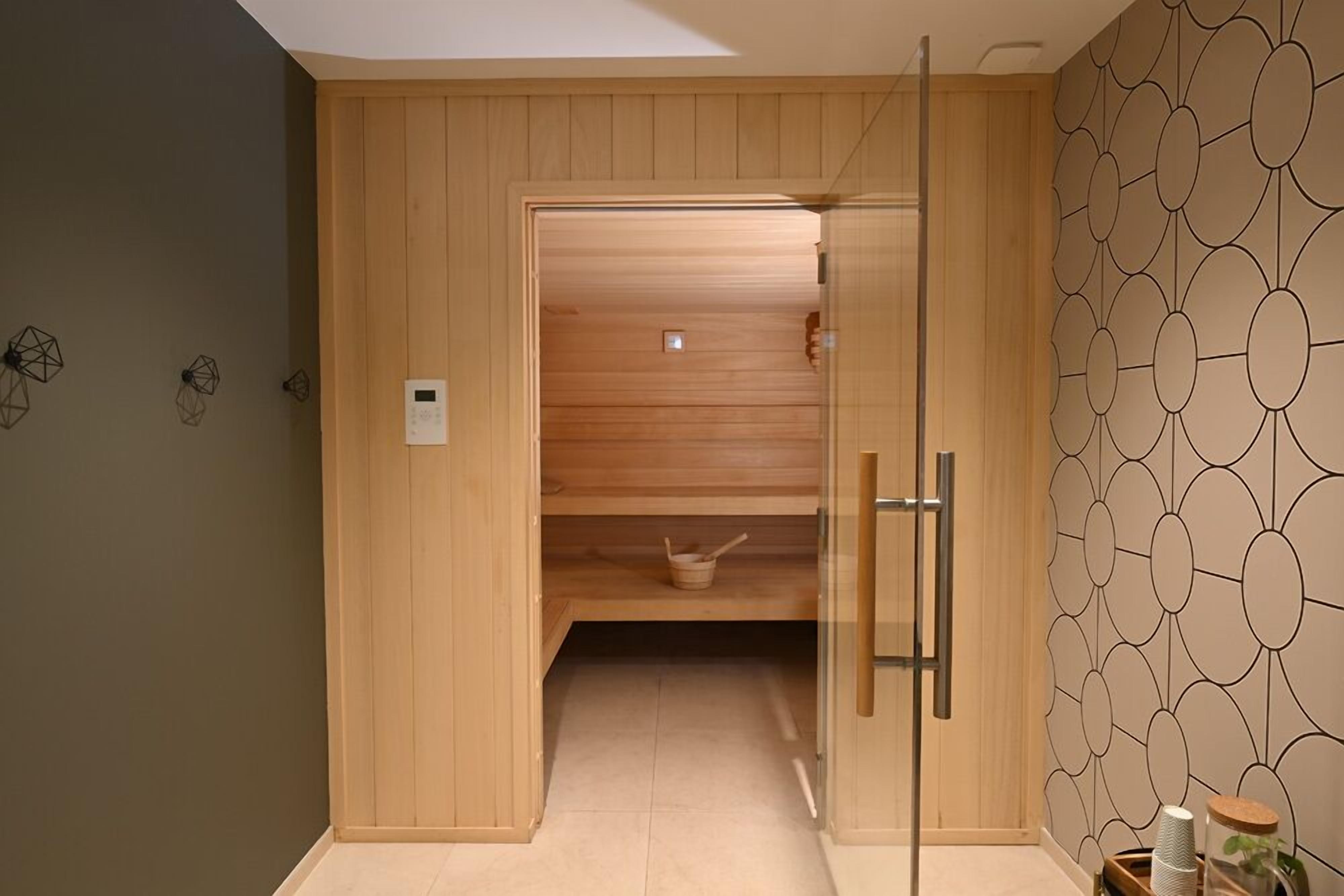 Un sauna de madera con puerta de vidrio, panel de control y pared con diseño.