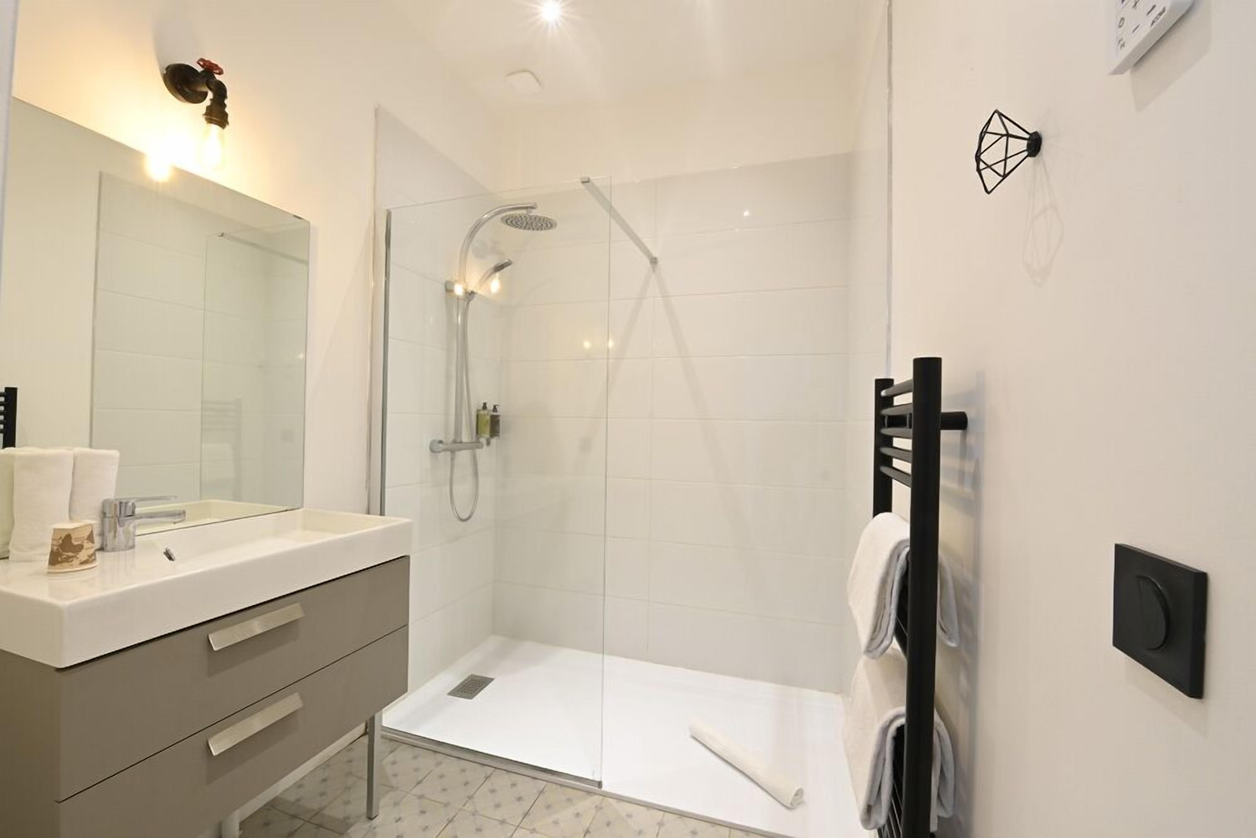 A modern bathroom with a glass shower enclosure, a white sink with a mirror, and a towel rack.