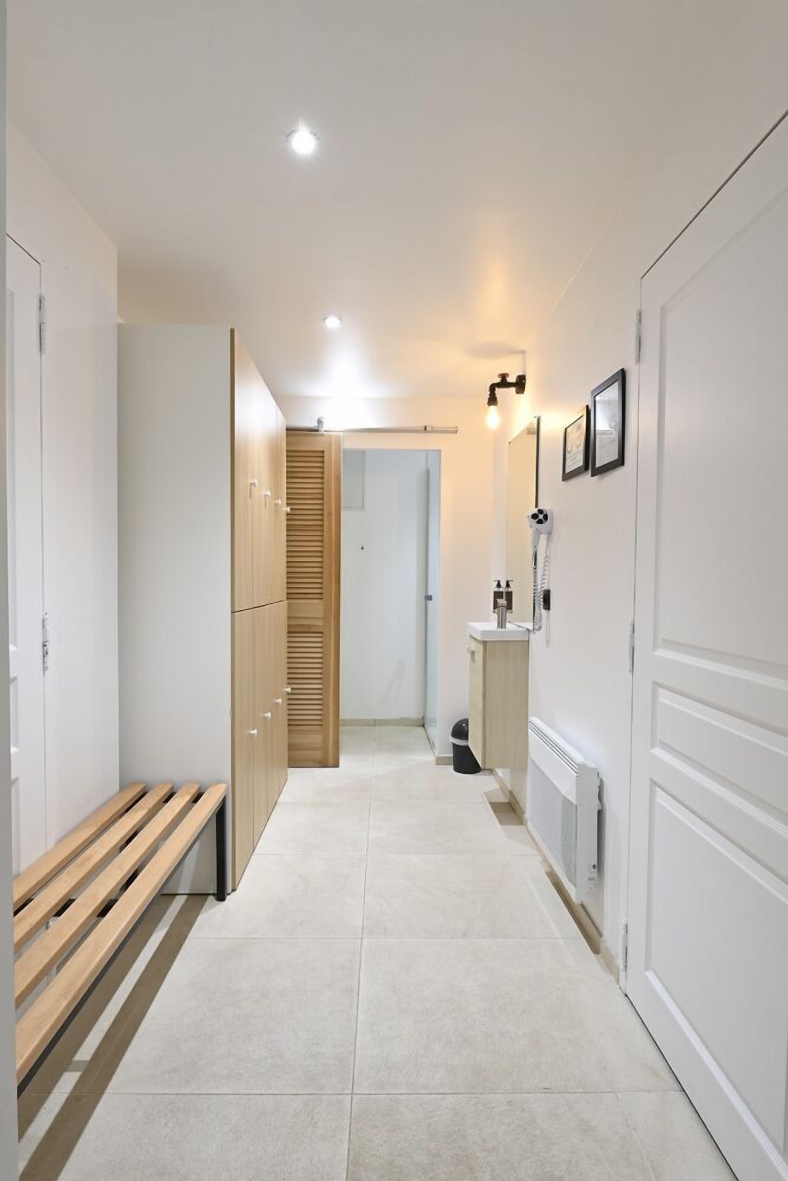 Un couloir avec un banc, des casiers en bois, un lavabo et un téléphone.
