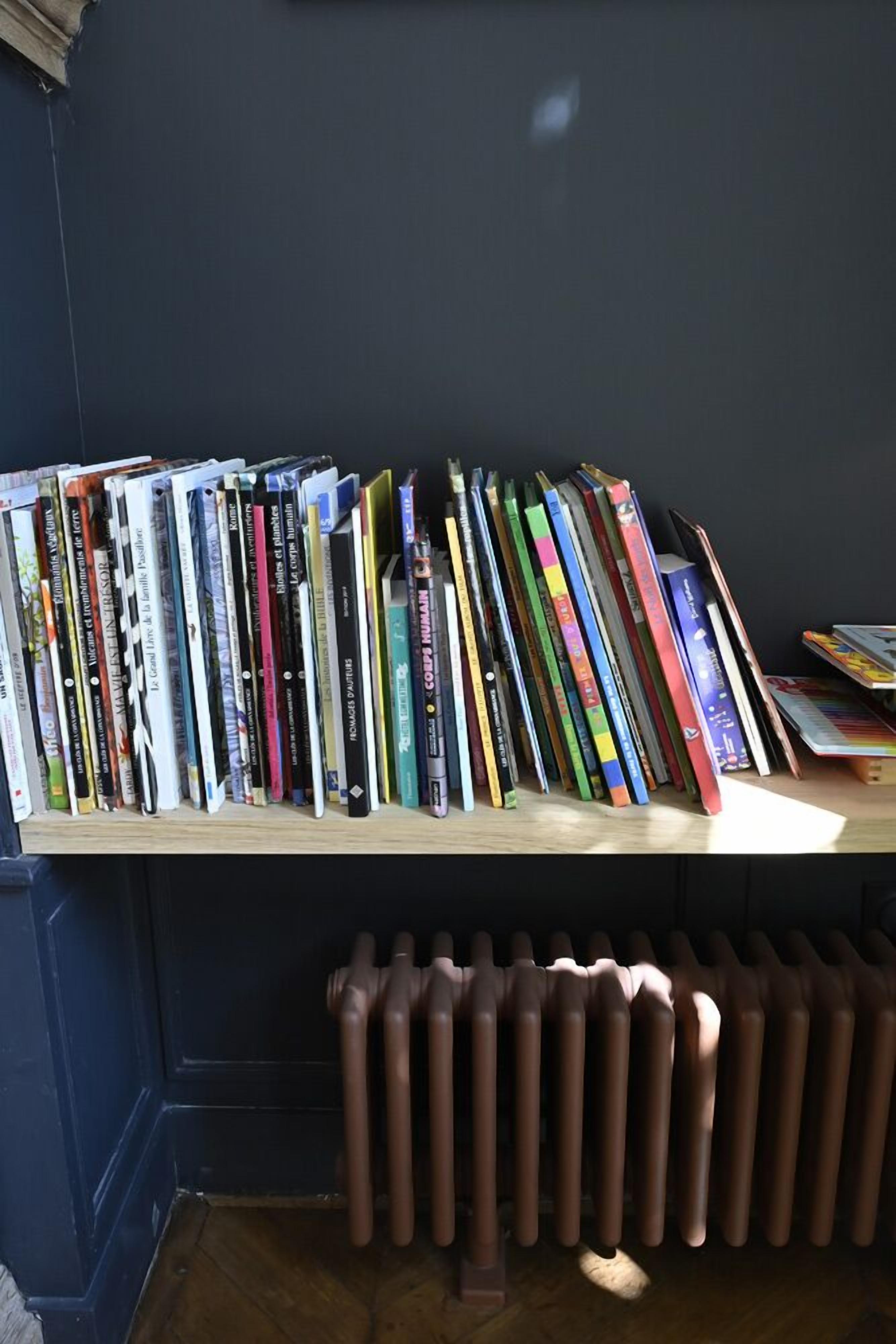 Une bibliothèque remplie de livres et un radiateur en dessous.
