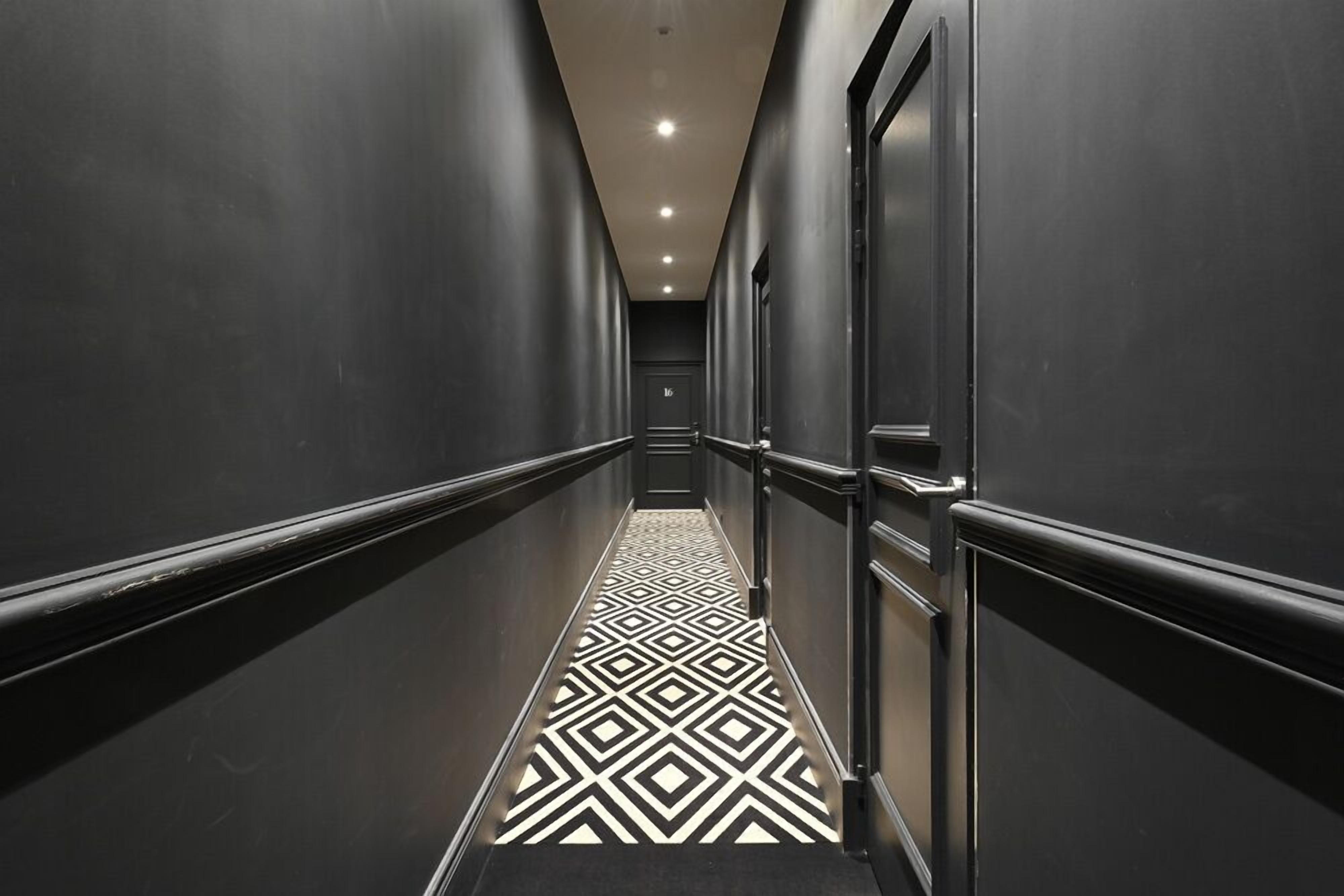 A long, narrow hallway with a geometric patterned floor and dark walls.