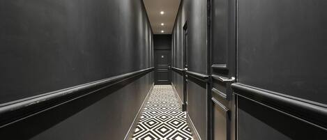 A long, narrow hallway with a geometric patterned floor and dark walls.