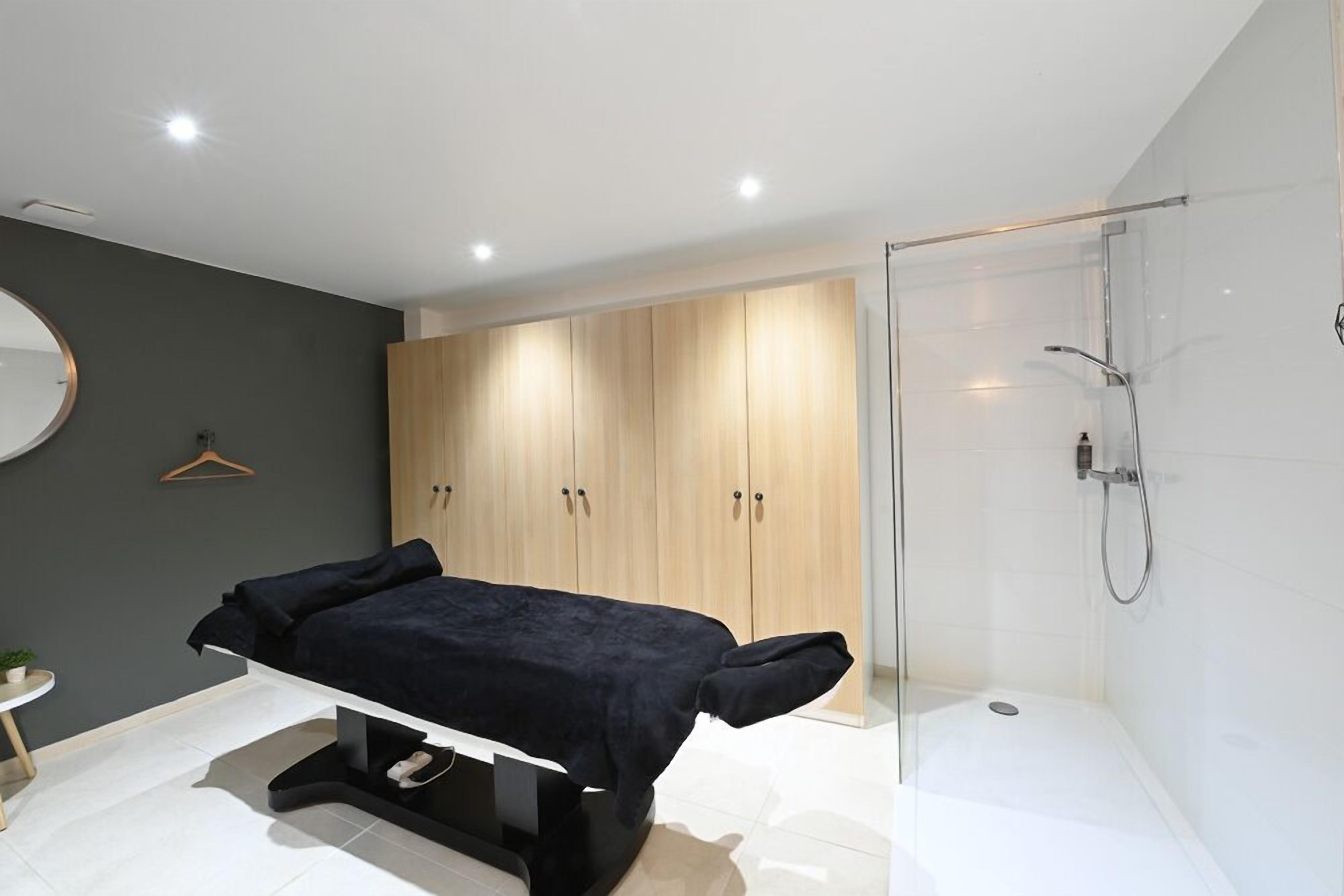 A modern bedroom with a bed, a bedside table, a small round mirror, and a wardrobe.