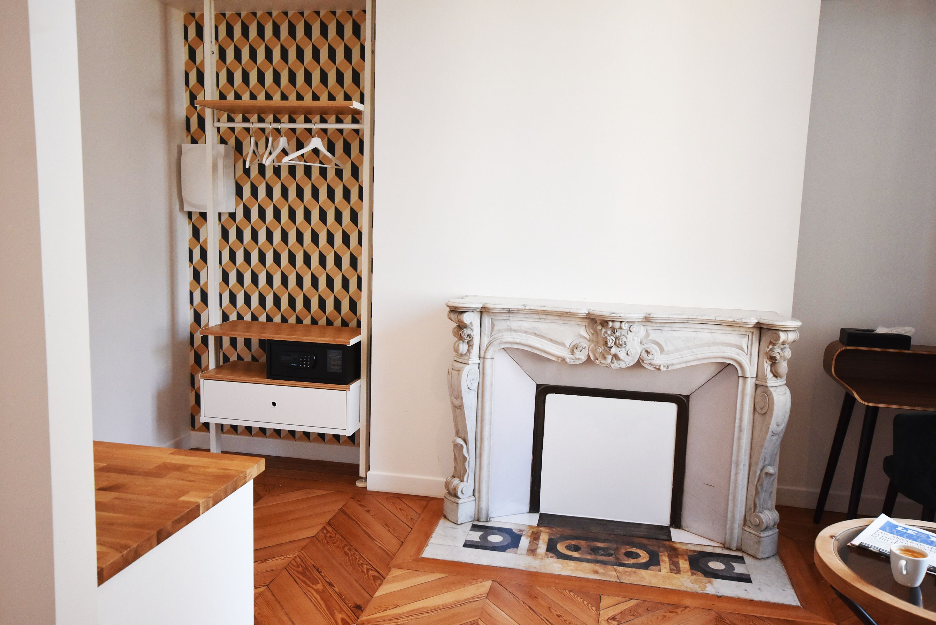 A room with a fireplace, a wooden floor, a patterned wall, and a small table with a cup and a menu.
