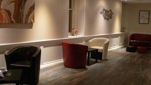 A modern lobby with a wooden floor, a red and white armchair, a black leather chair, and a small table with a cup. - The Home Arms Guesthouse (Eyemouth)
