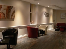 Un vestíbulo moderno con suelo de madera, un sillón rojo y blanco, un sillón de cuero negro y una pequeña mesa con una taza.