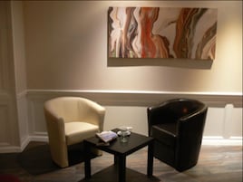 Una habitación con dos sillas, una mesita y un cuadro abstracto grande en la pared.