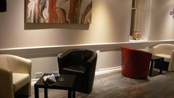 A modern lounge area with a black leather chair, a red chair, and a small table with a cup and papers.