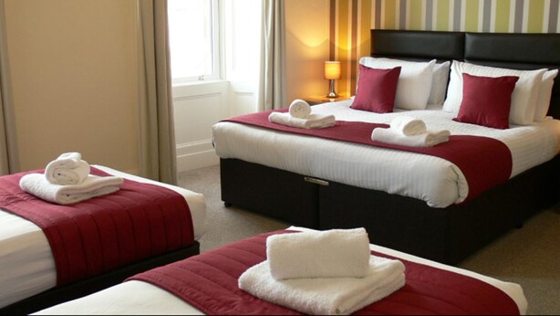 A hotel room with two beds, each with a red bedspread and white linens, and a nightstand with a lamp. - The Home Arms Guesthouse (Eyemouth)