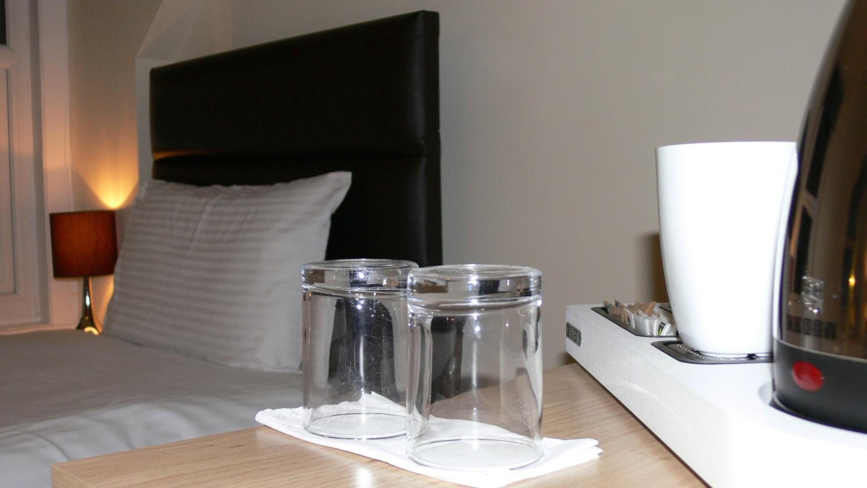 A hotel room with a bed, a bedside table, and a lamp.