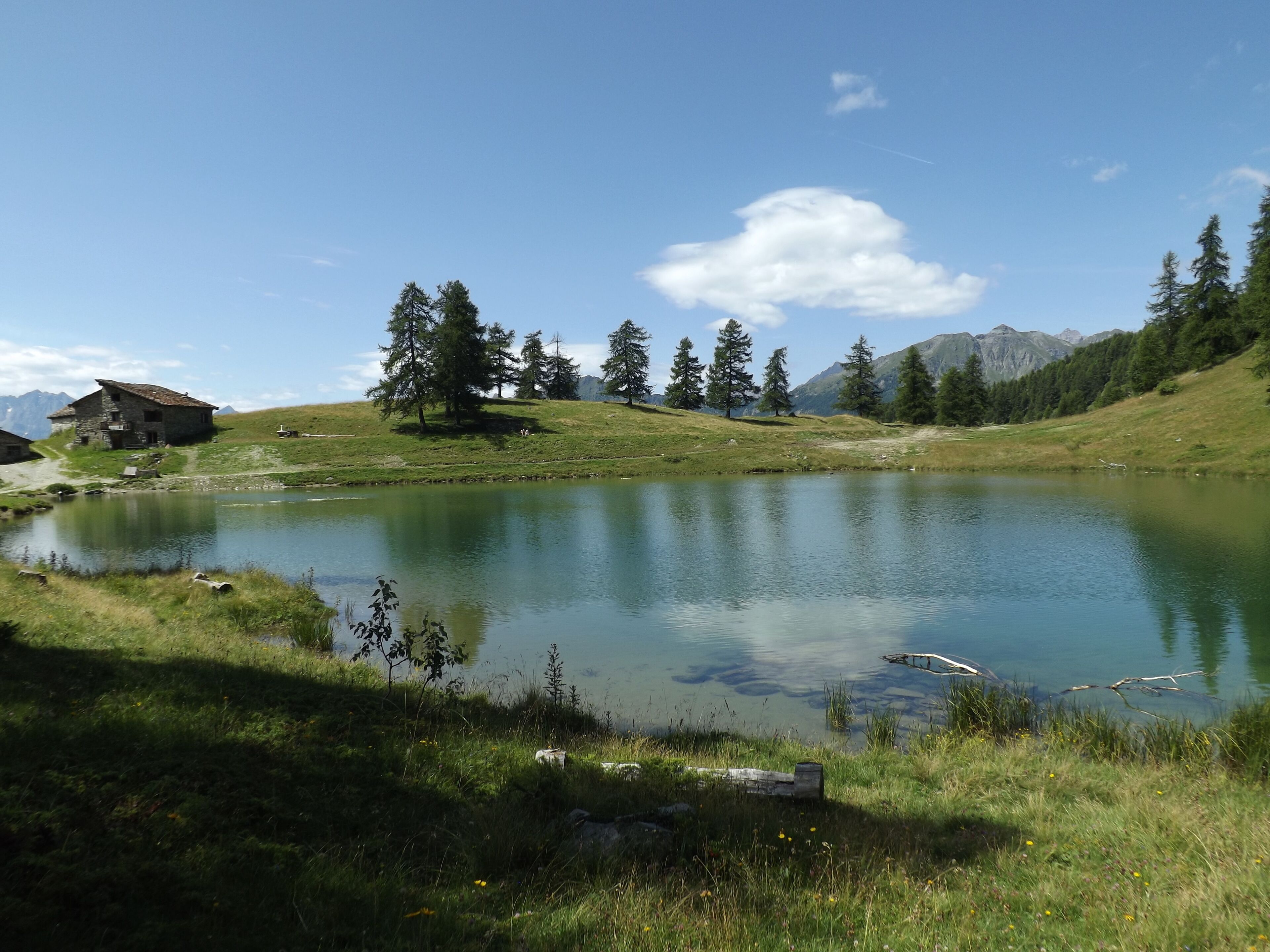 A rustic stone house by a calm lake surrounded by trees and mountains.