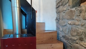 Una estufa de leña, escaleras de madera y una pared de piedra.
