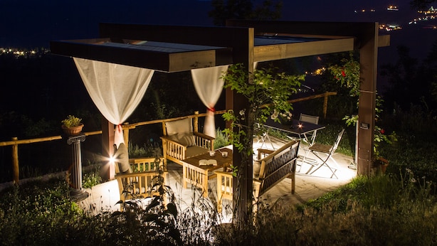 Una terraza de madera al aire libre con una mesa y sillas, rodeada de plantas y vista a la montaña de noche.