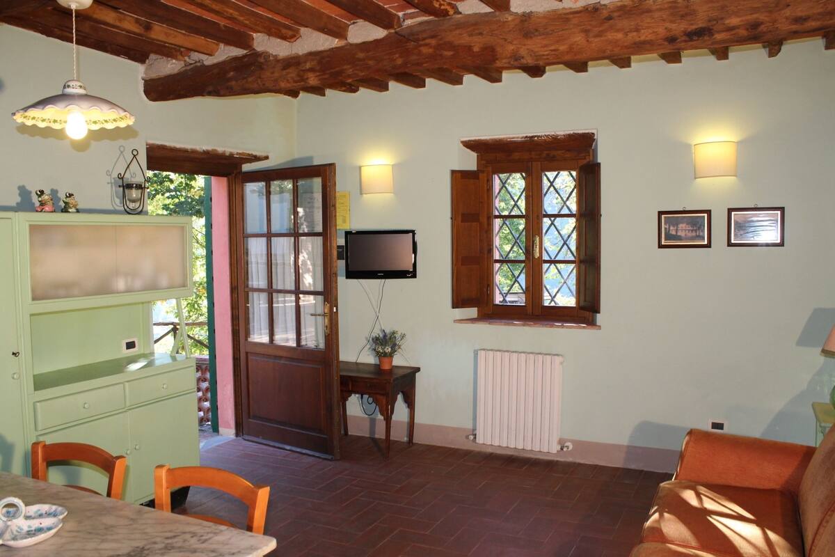 Una habitación acogedora con techo de madera, un armario verde, una mesa con sillas, un ventanal y un televisor.