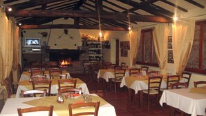 A restaurant with multiple tables and chairs, a fireplace, and a television screen. - Agriturismo la Torre (Bagni di Lucca)