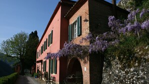 A traditional red brick building with green shutters, a stone archway, and purple flowering vines. - Agriturismo la Torre (Bagni di Lucca)
