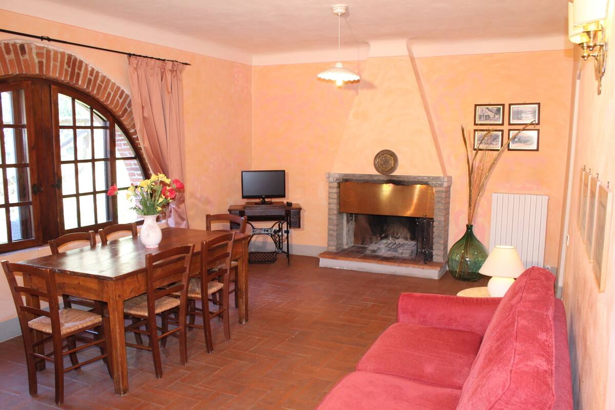 Una sala de estar con chimenea, televisor, mesa de comedor con sillas y un sofá rojo.