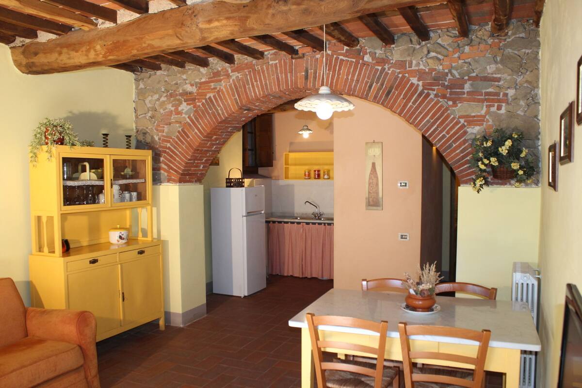 Una cocina rústica con un arco de ladrillo, armarios de madera y una mesa de comedor con sillas.