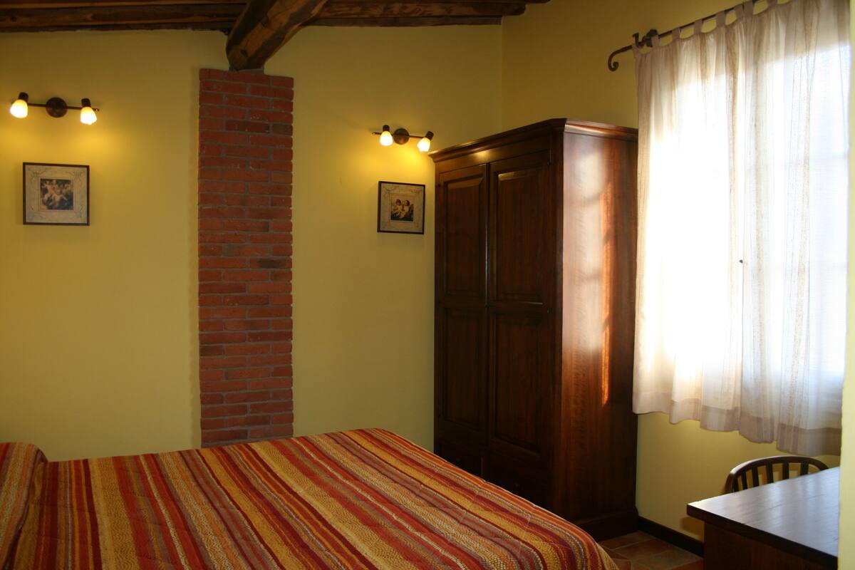Una habitación con una cama, un armario de madera, un muro de ladrillo y dos lámparas fijadas a la pared.