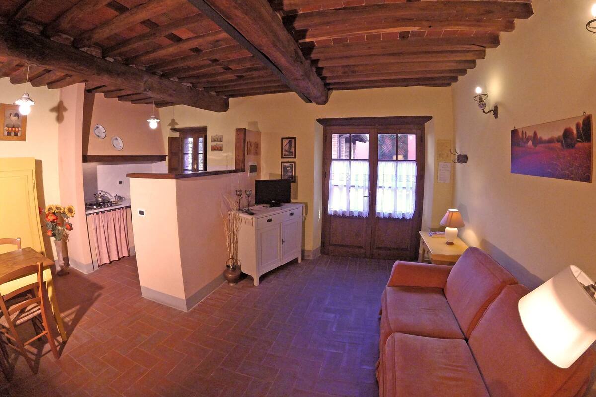 Una sala acogedora con sofá, una mesa de comedor y una zona de cocina con refrigerador y televisor.
