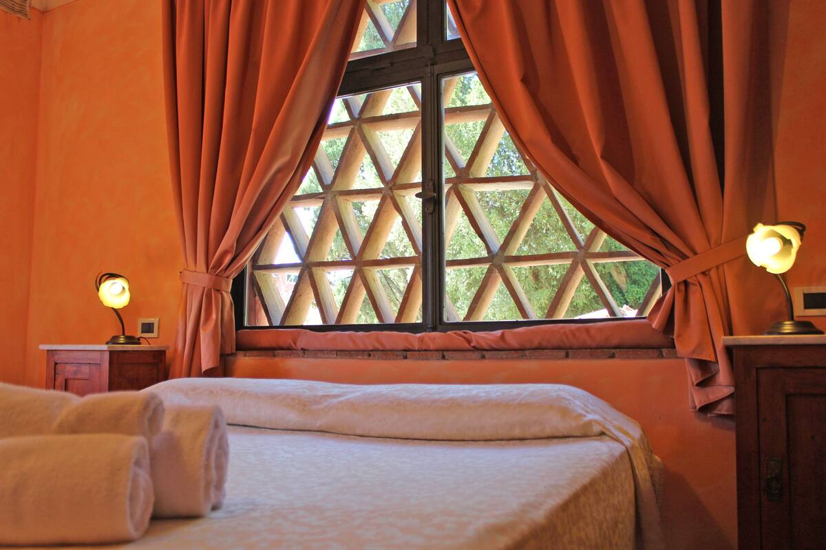 Una habitación con una cama, una ventana con cortinas y dos lámparas de noche.