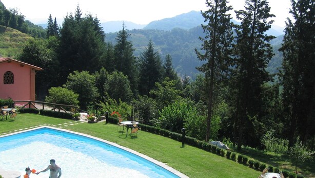 A swimming pool with a man and a child playing, surrounded by a well-maintained lawn and trees. - Agriturismo la Torre (Bagni di Lucca)